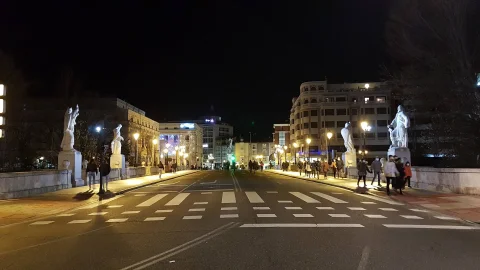 Calzada urbana nocturna del puente flanqueada por las esculturas cidianas iluminadas y peatones