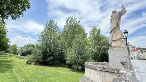 Estatua de Don Jerónimo alzada sobre el pretil de piedra con amplia panorámica de la ribera verde