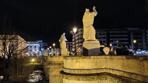 Estatua nocturna en contrapicado de Don Jerónimo sobre el tajamar del puente con el cauce iluminado debajo