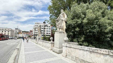Perspectiva peatonal del puente con las estatuas cidianas sobre pedestales y arboleda del cauce fluvial