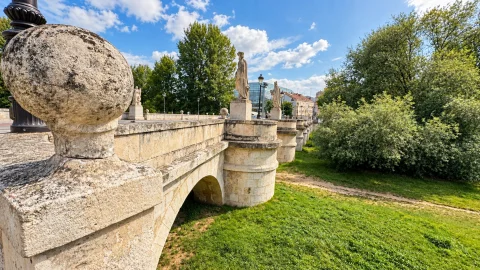Remate esférico de piedra en primer plano con perspectiva de los arcos, estatuas cidianas y ribera ajardinada
