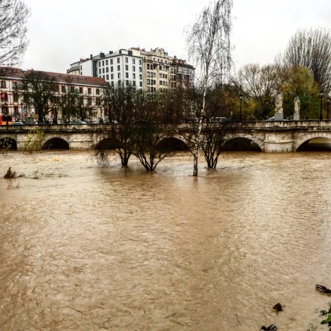 Río desbordado con caudal marrón cubriendo casi por completo los arcos de un puente de piedra antiguo