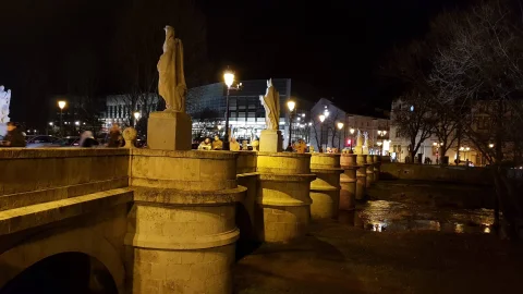 Vista nocturna iluminada de los tajamares del puente con las esculturas y reflejos en el río Arlanzón