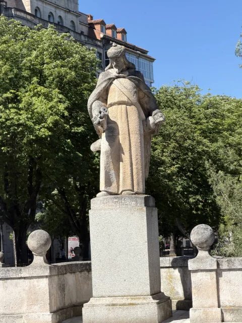 Escultura de Abengalbón de cuerpo entero sobre pedestal de granito flanqueado por los bolardos del puente