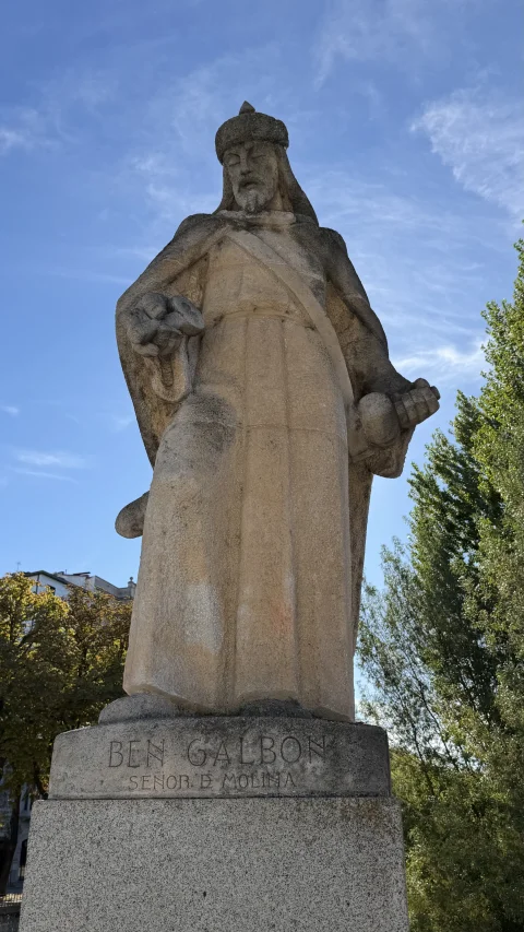 Estatua de piedra de Ben Galbón con túnica y gorro sobre un pedestal