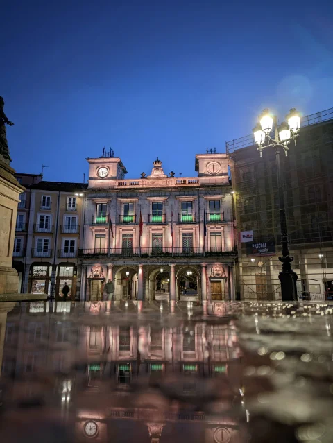 Vista nocturna del Ayuntamiento de Burgos iluminado reflejándose sobre un charco
