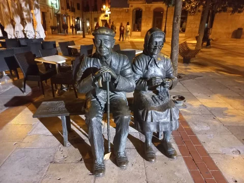 Los Abuelos sentados de Burgos de noche, el matrimonio de bronce en su banco con las terrazas al fondo