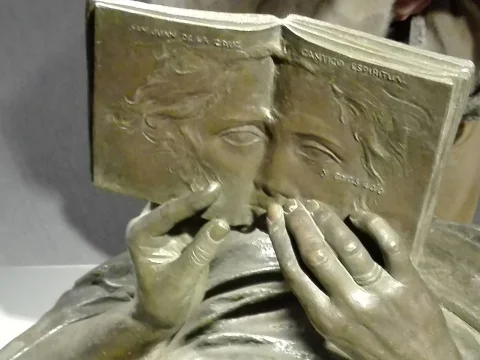 Primer plano de manos de bronce sujetando un libro esculpido con relieves de rostros en sus páginas