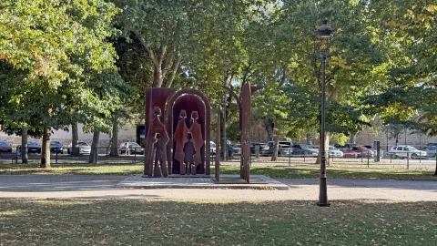 Vista del monumento con farola clásica y entorno ajardinado