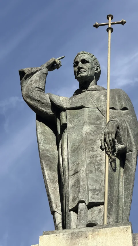 Detalle de la estatua de bronce de Santo Domingo de Guzmán portando un rosario y una cruz alta con la mano levantada