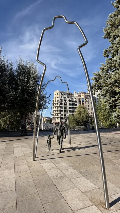 Estructura de arcos metálicos enmarcando las figuras de bronce de un homínido adulto y un niño caminando de la mano