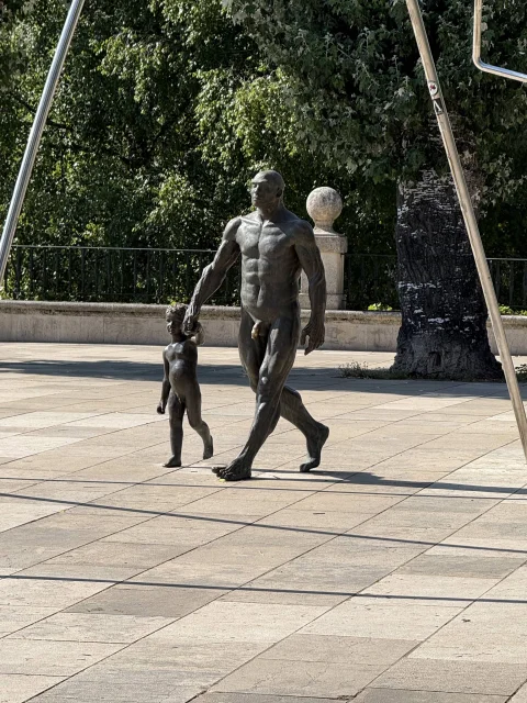 Plano entero de las esculturas de bronce de un homínido y un niño avanzando de la mano