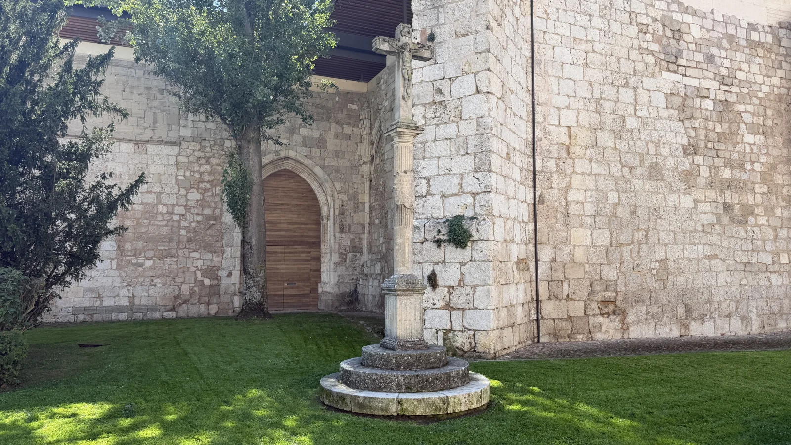 Crucero de la Plaza de San Juan de Burgos sobre el césped, junto al muro de sillería del monasterio