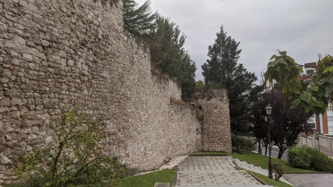 Paseo pavimentado en pendiente junto a la muralla de piedra y torres defensivas
