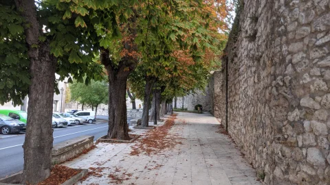 Paseo peatonal cubierto de hojas secas otoñales junto al lienzo de la muralla