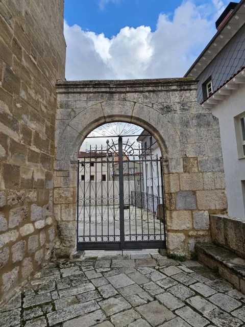 Arco de piedra con puerta de hierro forjado que da entrada a un patio arbolado adyacente al templo