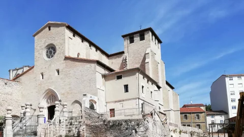 Fachada principal de piedra de la iglesia con rosetón superior, portada gótica y torre de campanas