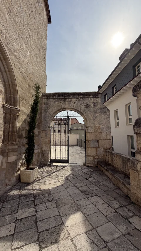 Arco de piedra con verja de hierro que da paso al patio interior iluminado por la luz del sol