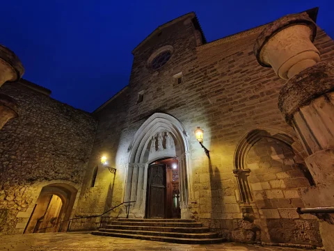 Vista nocturna iluminada de la fachada de piedra y la portada gótica con su portón abierto