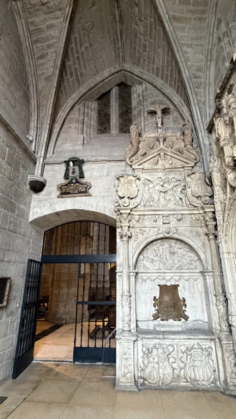 Entrada con cancela de hierro forjado bajo arco ojival junto a un sepulcro monumental renacentista