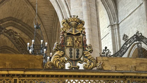 Escudo heráldico tallado en madera policromada con corona, yelmo y motivos de castillos y bandas