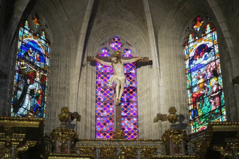 Escultura de Cristo en la cruz situada en el ábside flanqueada por vidrieras góticas de vivos colores