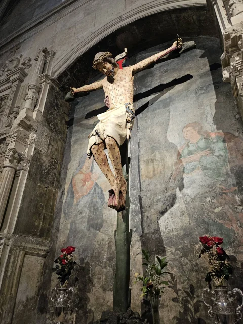 Plano en ángulo de la imagen esculpida de Cristo crucificado con detalles policromados de llagas y faldellín de tela