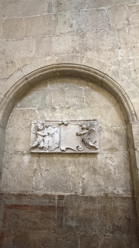 Relieve de putti sosteniendo blasón en un arcosolio