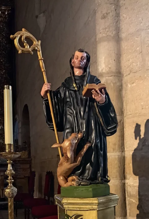 Talla policromada de San Gil con hábito negro, báculo pastoral dorado, libro abierto y la cierva a sus pies