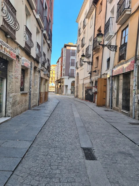 Calle estrecha empedrada con edificios tradicionales a ambos lados, farolas de hierro y comercios locales