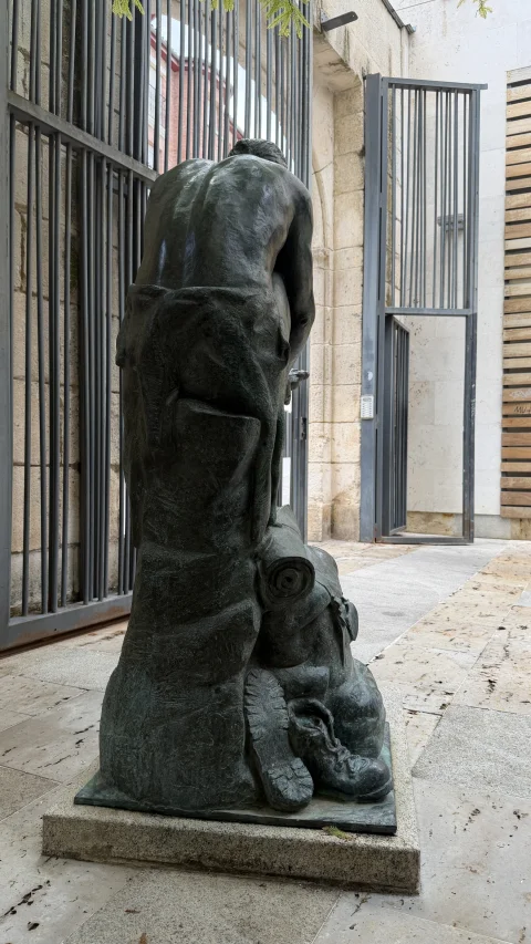 Espalda y detalles traseros de la estatua del peregrino descansando junto a sus botas de montaña