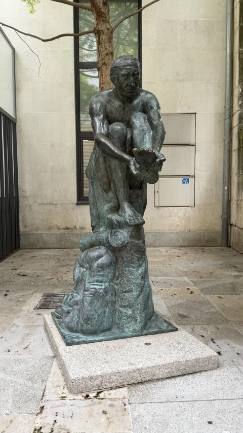 Figura de bronce de un peregrino sentado revisando su pie herido sobre un pedestal de granito