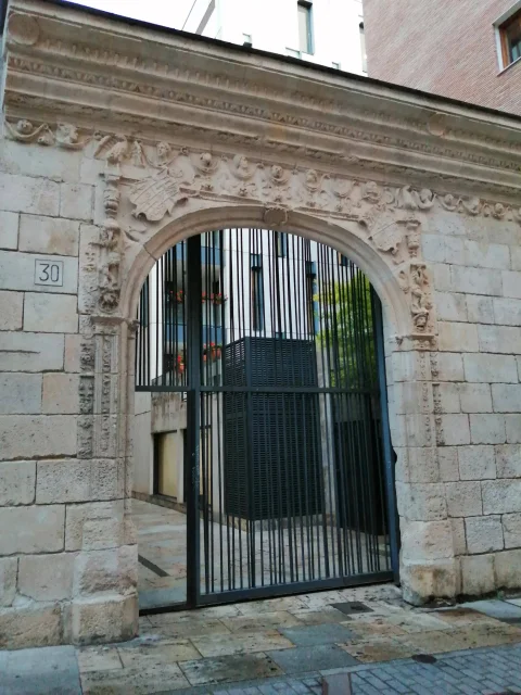 Portada auxiliar de piedra tallada con relieves platerescos y una gran reja metálica en el número 30 de la calle