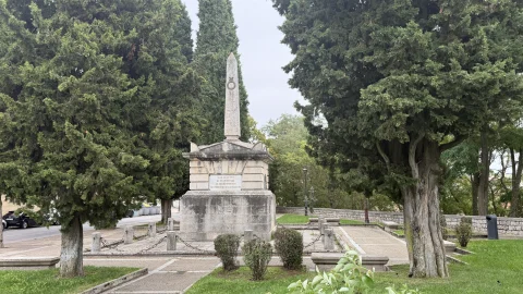 Monumento conmemorativo de piedra con obelisco situado entre altos cipreses