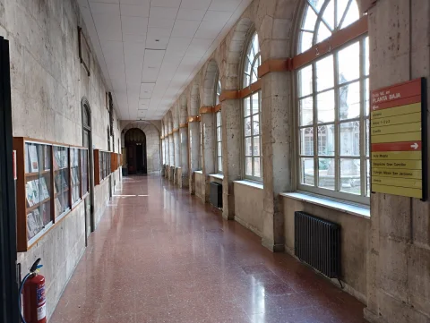 Vista del pasillo de arcos de piedra con vitrinas de libros y panel direccional en la Facultad de Teología
