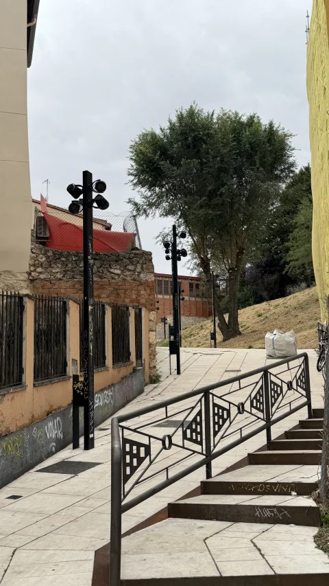 Subida de peldaños con barandilla metálica, farolas oscuras de diseño moderno y arbolado al fondo en la Calle Álvar Fáñez