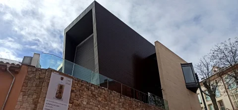 Primer plano del bloque superior de tonos oscuros del edificio emergiendo tras un muro de mampostería de piedra