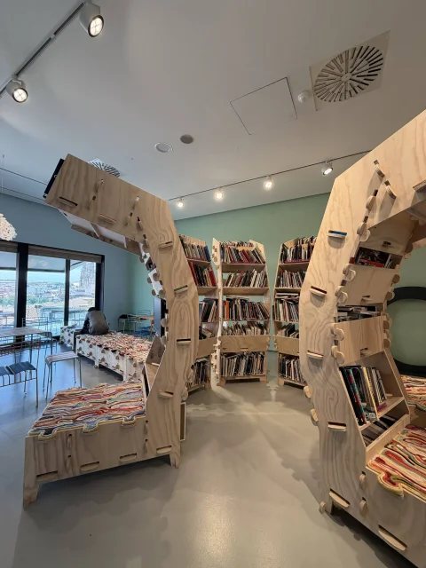 Espacio de lectura con estanterías curva de madera contrachapada y asientos acolchados con textiles multicolores