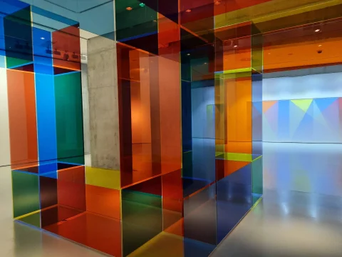 Estructura geométrica hecha con paneles de metacrilato en tonos azules, naranjas y amarillos en el interior de la sala expositiva