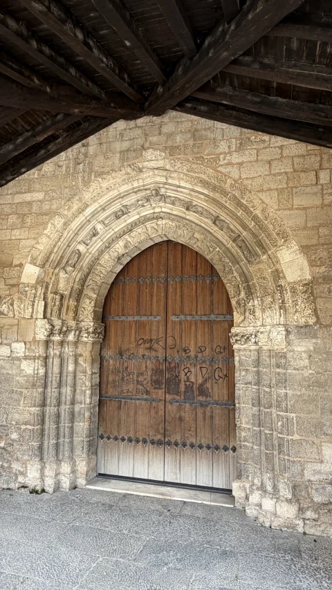 Portada gótica de arcos apuntados con puerta de madera tachonada resguardada bajo el pórtico exterior