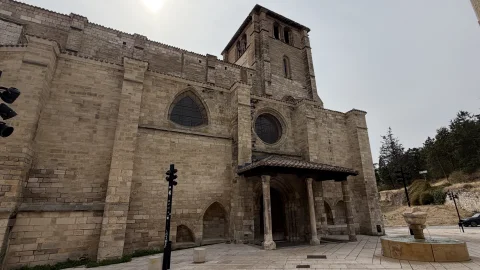 Vista lateral de los muros de sillería de la iglesia con su pórtico de entrada de madera y la torre del campanario al fondo
