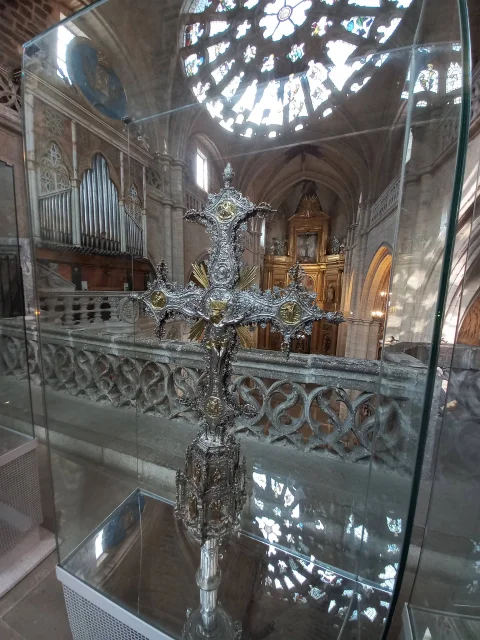Cruz procesional gótica de plata expuesta en una urna de cristal con la nave del templo al fondo
