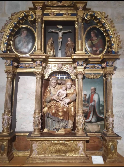 Retablo dorado con relieve central de Santa Ana, la Virgen y el Niño y pintura lateral de un clérigo