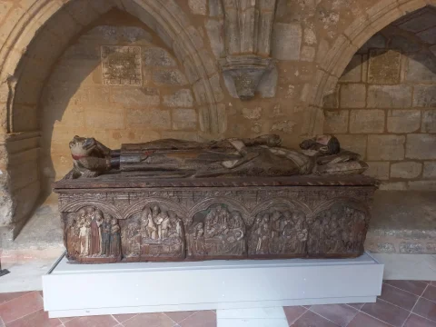 Sepulcro medieval de piedra tallada con figura yacente y relieve de figuras religiosas en el frontal