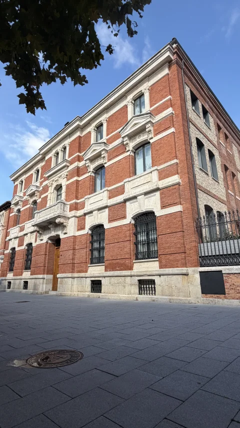 Perspectiva de tres cuartos del edificio histórico del Banco de España con fachada de ladrillo rojo y carpintería metálica