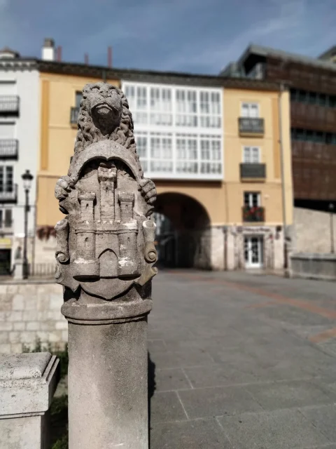 León y escudo del castillo de tres torres en el Puente de las Viudas de Burgos, con el Arco de San Juan al fondo