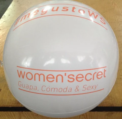 Balón de playa hinchable blanco con el logotipo naranja de women'secret sobre una mesa de madera