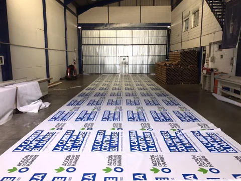 Bobinas de lona publicitaria impresas con el logotipo de La Carrera Contra el Hambre de Acción Contra el Hambre en taller