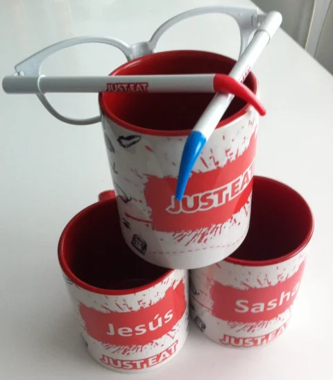 Juego de tazas cerámicas personalizadas con el nombre y logo de Just Eat junto a bolígrafos publicitarios